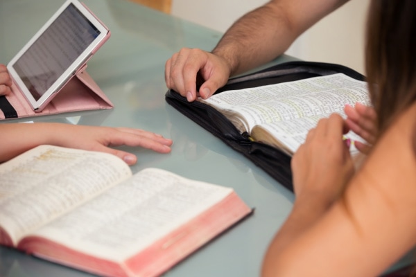 Bibles open on table with hands nearby
