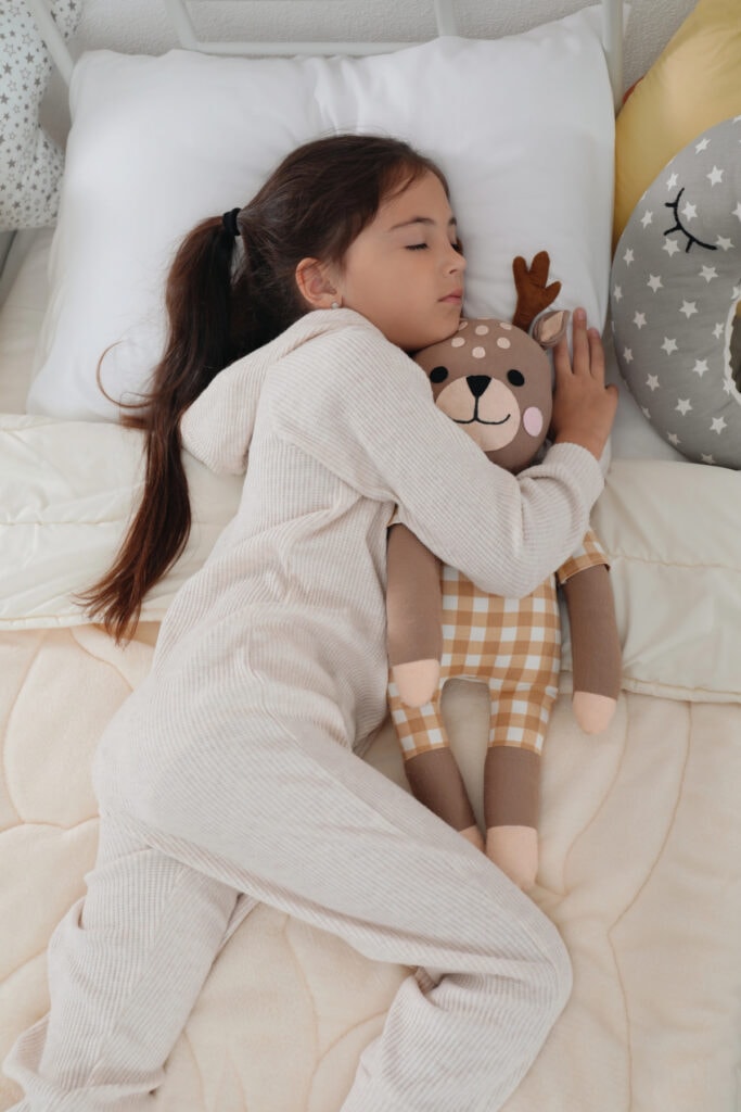 young girl laying in bed with a stuffed animal
