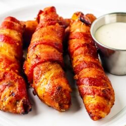 cooked bacon wrapped chicken on a white plate with some dip
