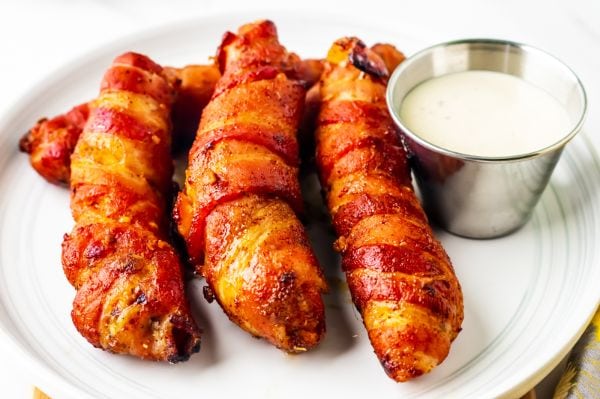 cooked bacon wrapped chicken on a white plate with some dip