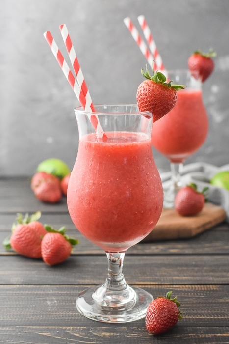 glass of strawberry daiquiri with 2 striped straws