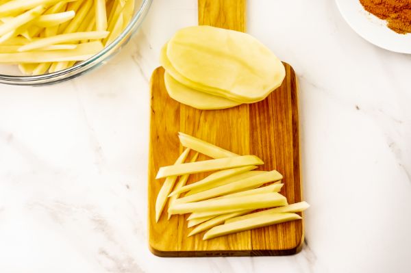 potato on a cutting board being cut into strips for fries