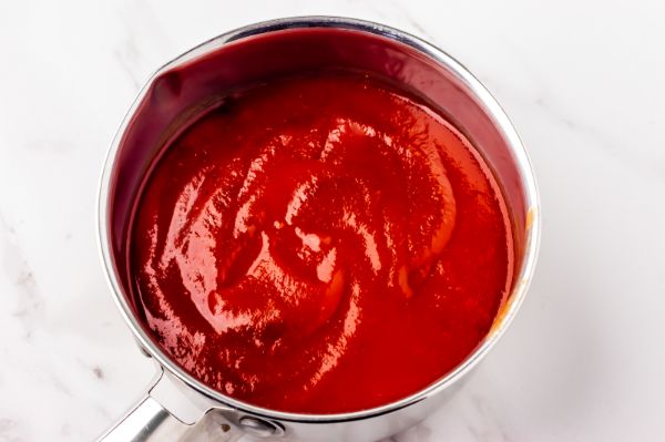 adding tomato sauce to saucepan while making enchilada sauce