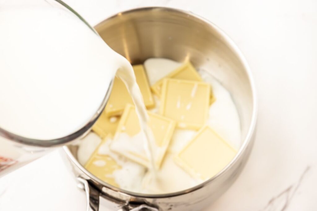 white chocolate squares in a silver pot with milk being poured into the pot