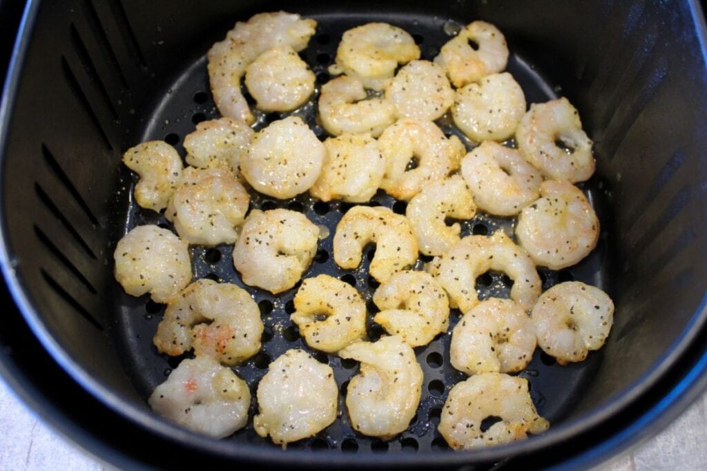 air fryer basket with lemon pepper seasoned shrimp in it