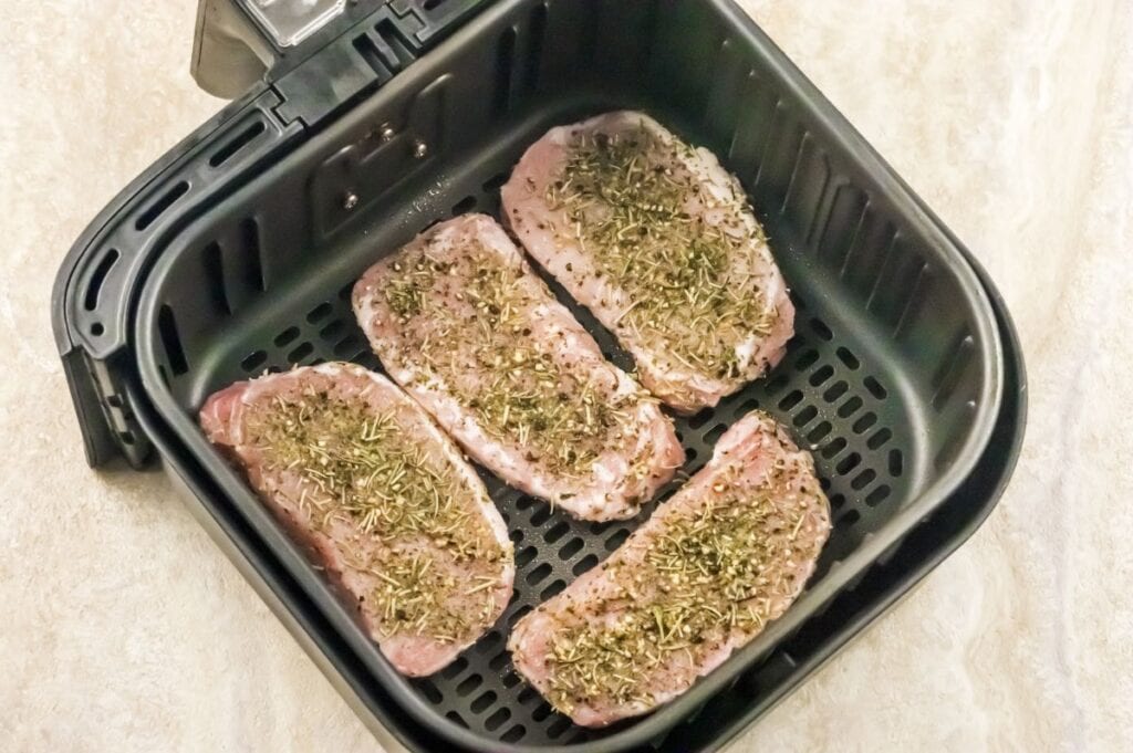 air fryer basket with seasoned boneless pork chops ready to cook