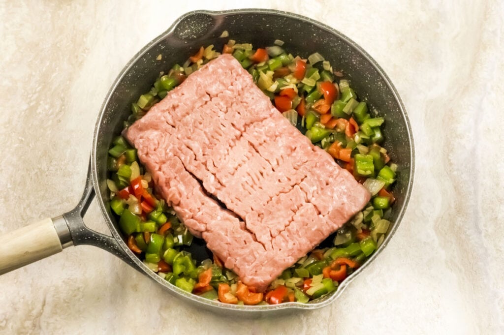 skillet with sauted vegetables and a pound of ground turkey ready to cook