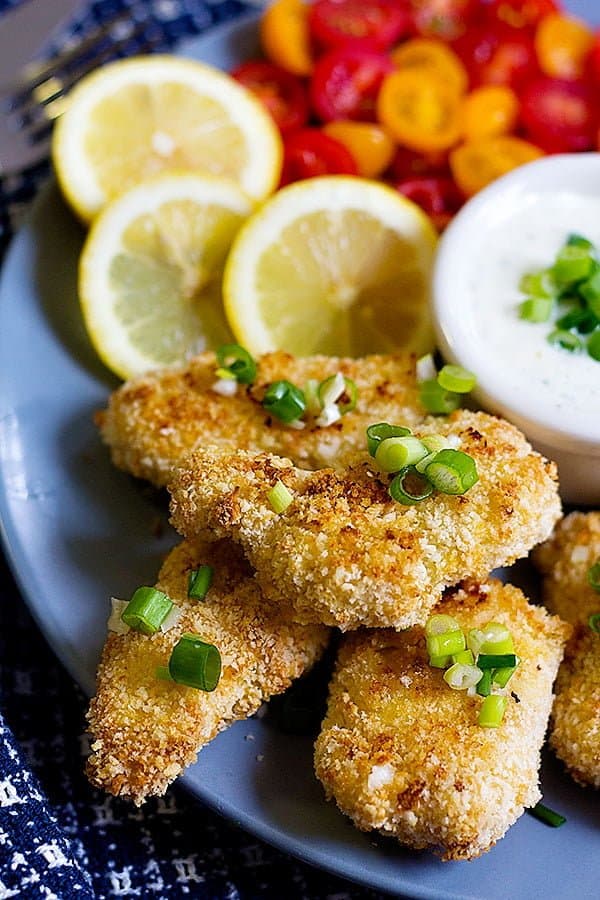 Baked chicken tenders on a plate with ranch and lemons