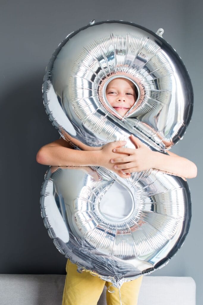 child hugging a huge silver number 8 inflated balloon