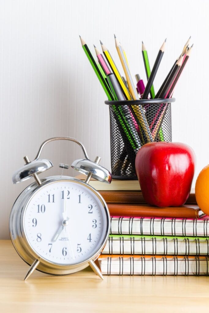 Alarm clock, apple, notebooks, and pencils