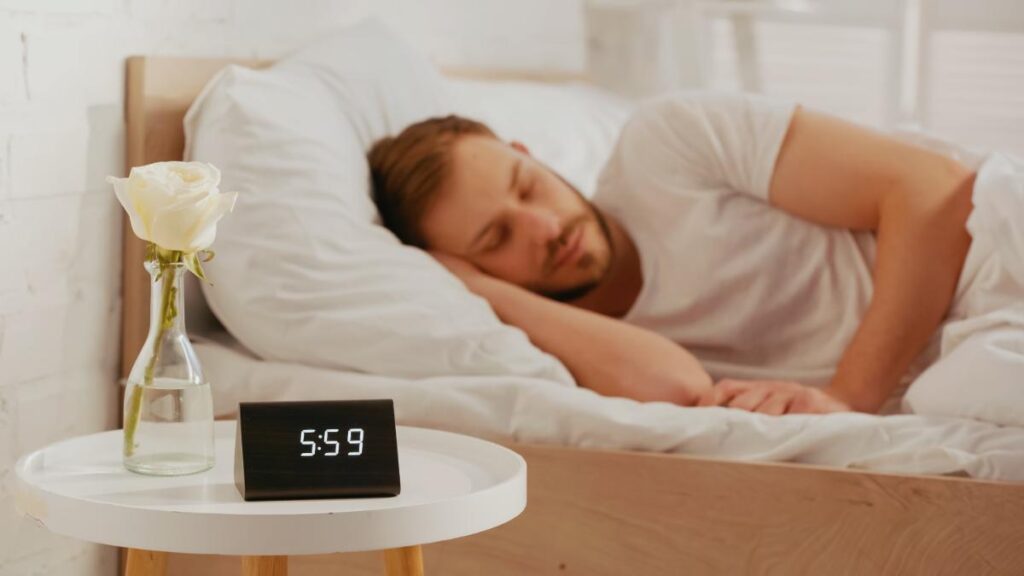 guy sleeping with an alarm clock beside him