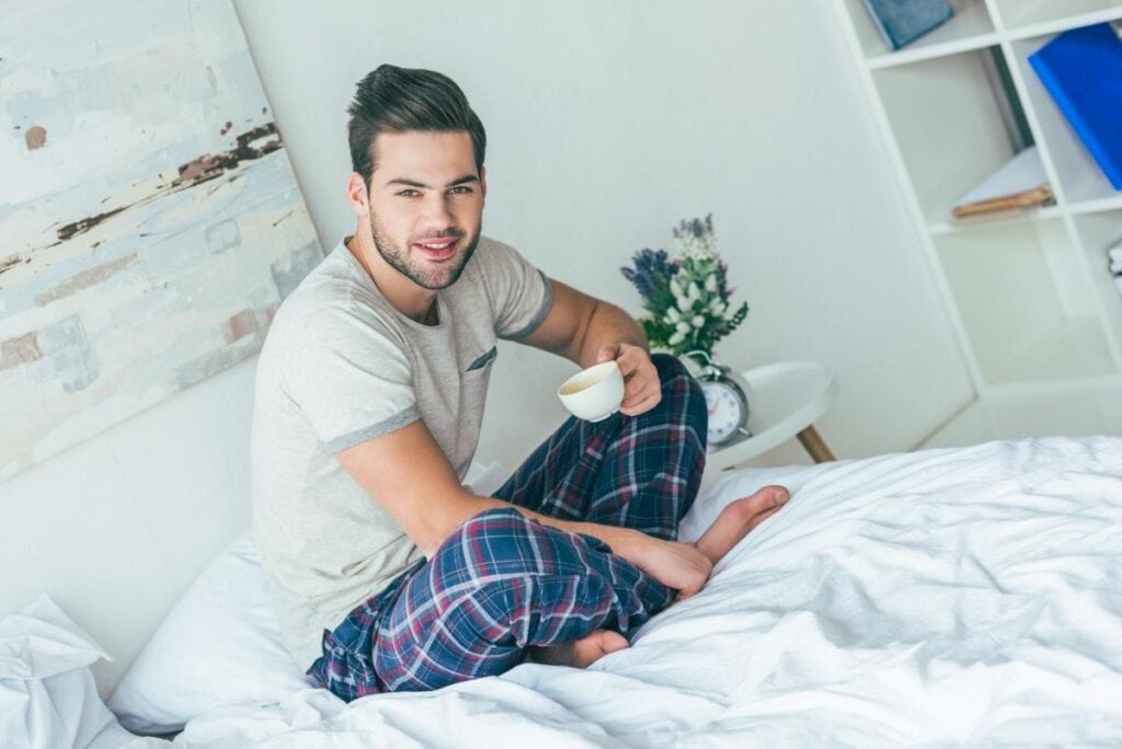 guy sitting on the bed while drinking coffee