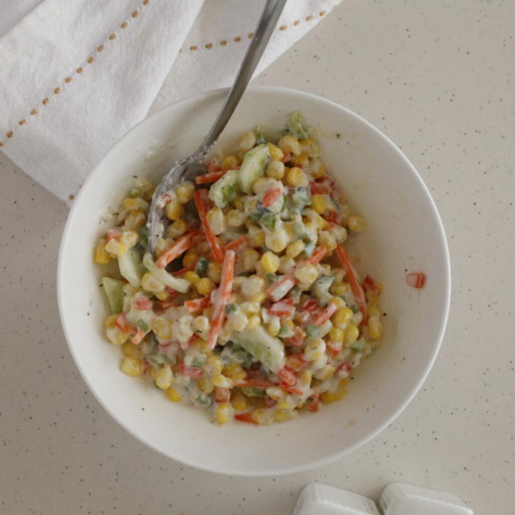mixing dressing with corn, cucumber, carrots, and bell pepper