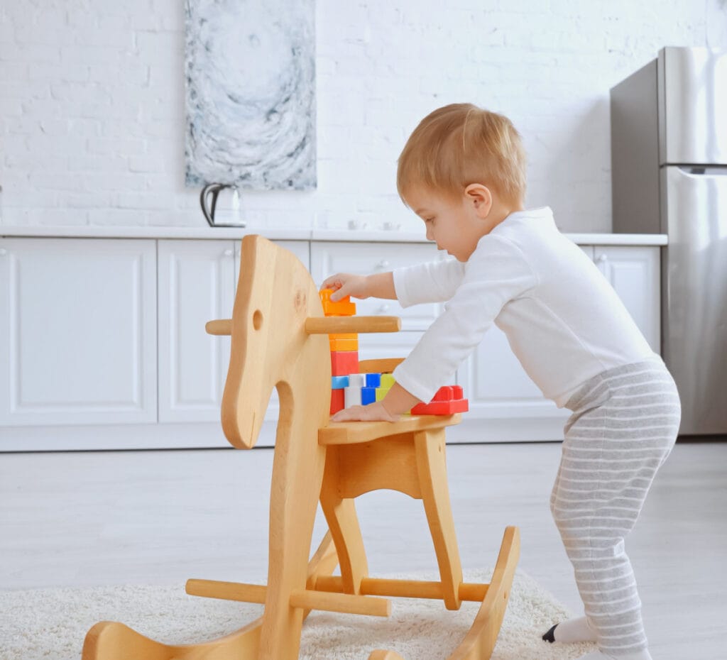 baby standing by wooden rocking horse