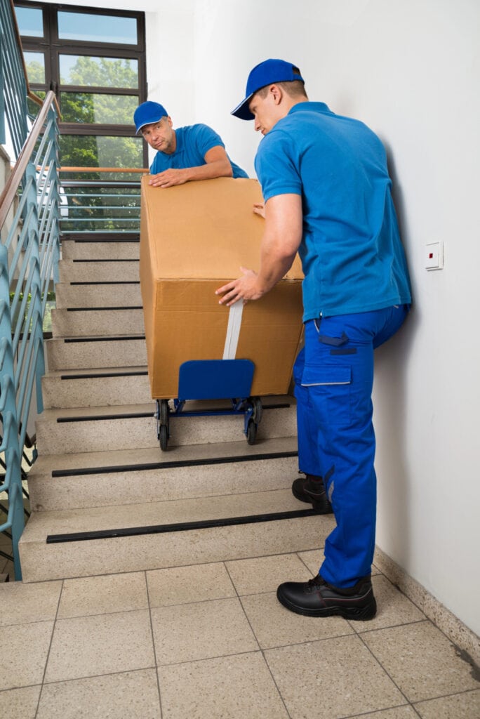 moving men carrying large box up stairs