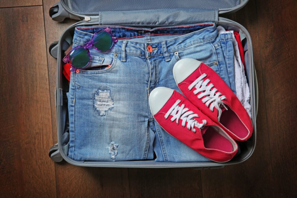 open suitcase full with jeans and red shoes on top