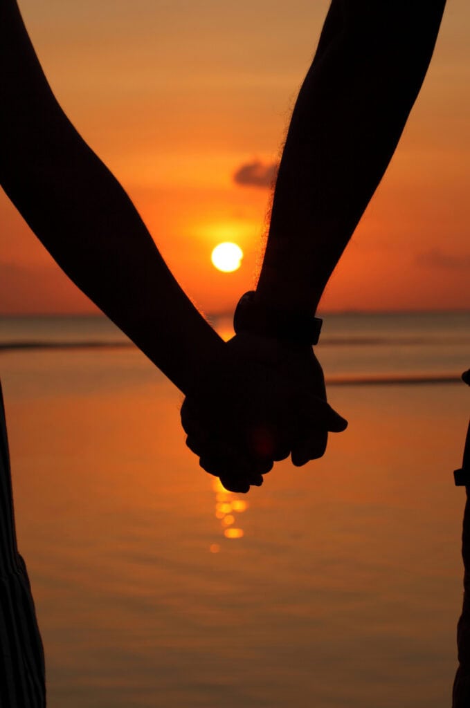 couple holding hands on beach at sunset
