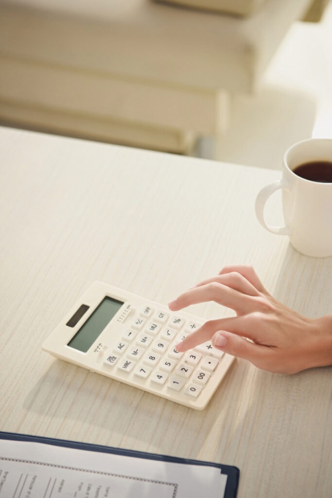 woman using calculator next to a cup of coffee at the table