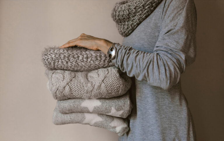 woman holding stack of sweaters